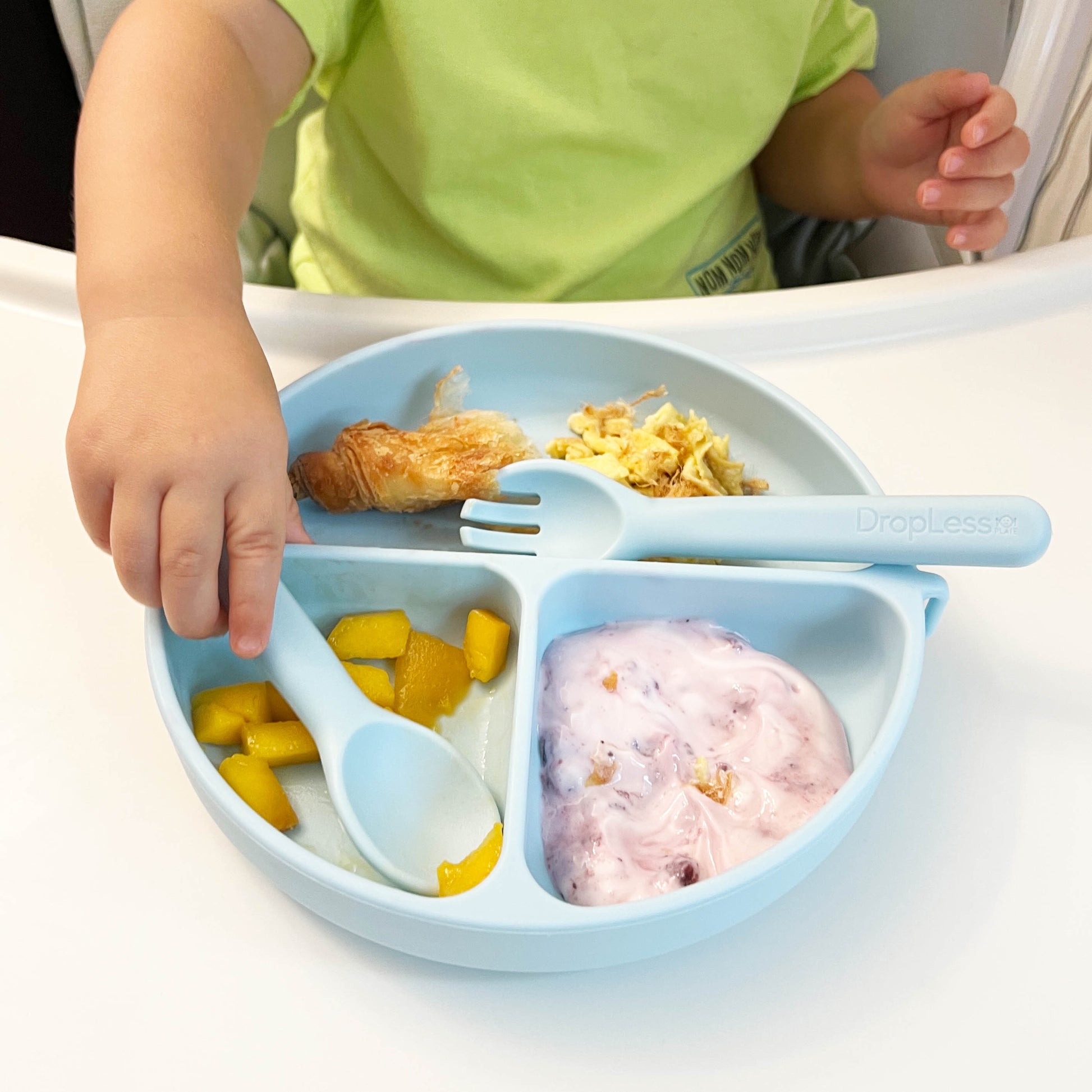 Child using a blue divided plate with utensils on a white table