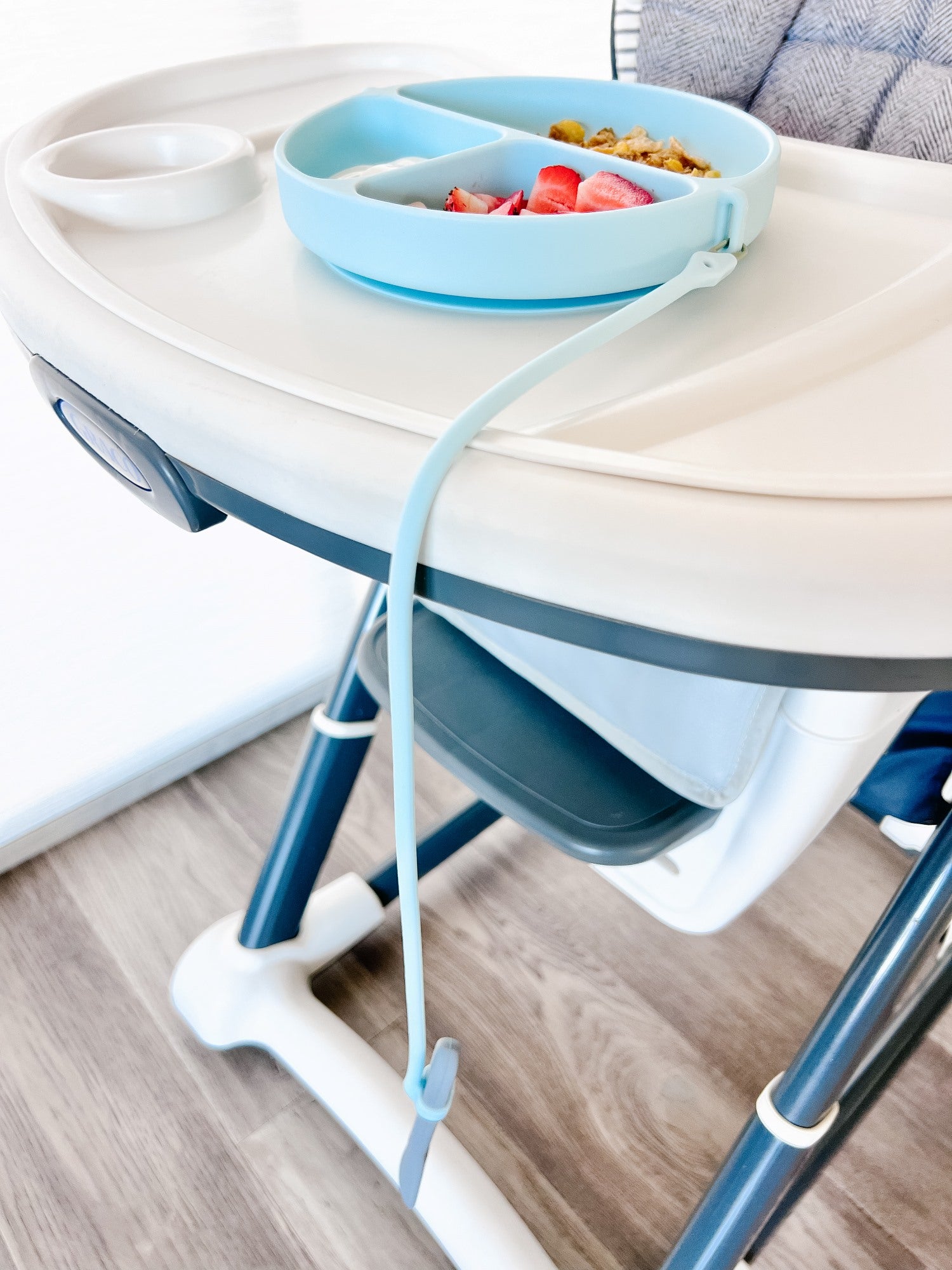 Dropless plate on a children's high chair with a tray holding food on a wooden floor.