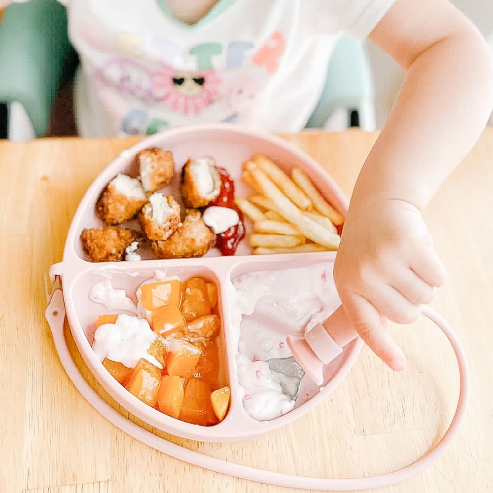 Close-up of toddler girl using a pink DropLess Plate, scooping yogurt with her spoon