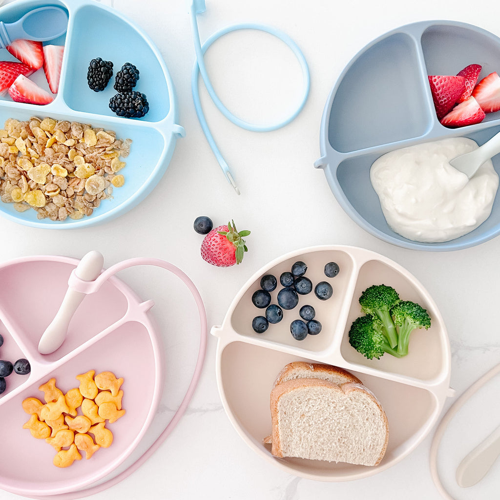 DropLess Plates in four different colors, each filled with food – toddler suction plates for self-feeding