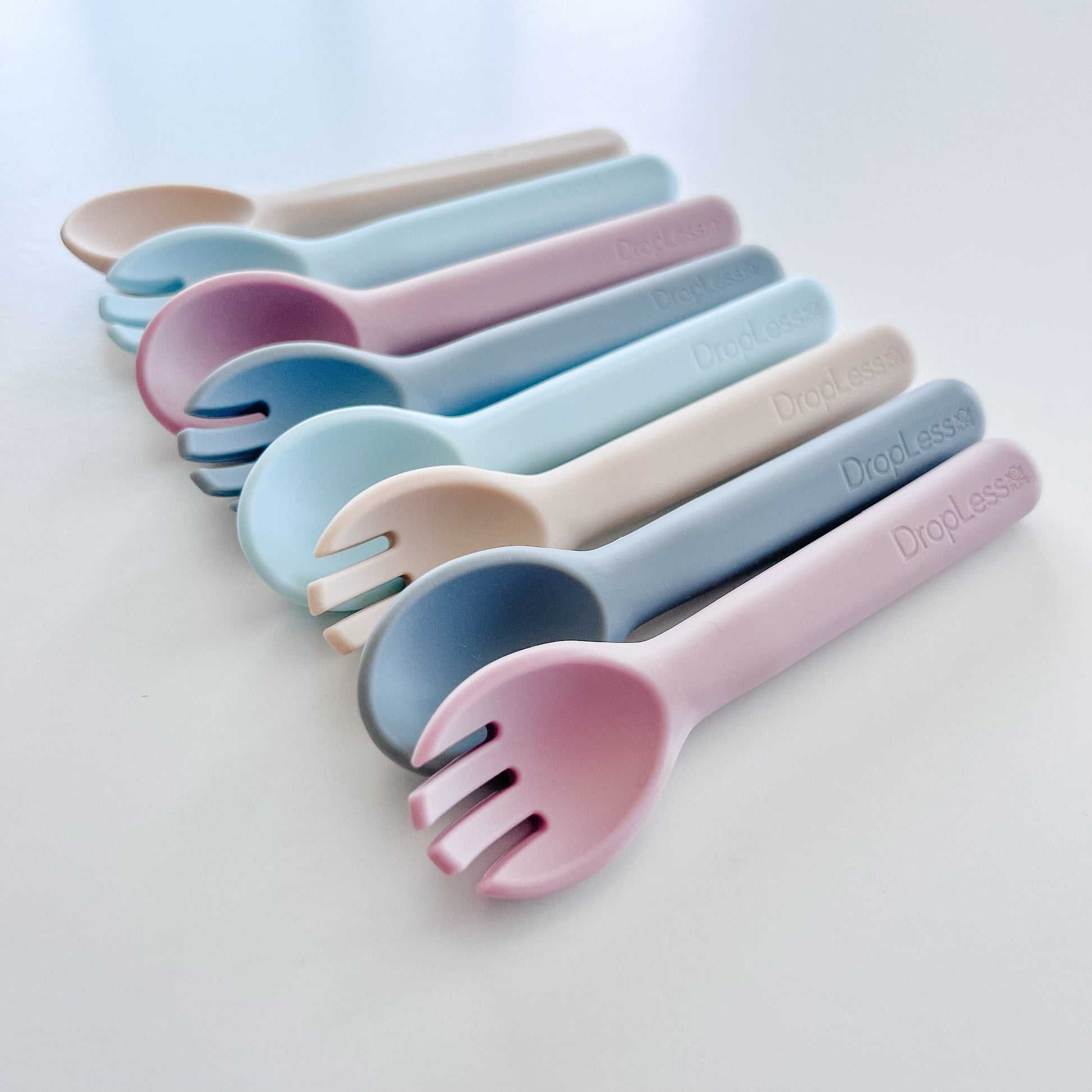 Set of colorful plastic forks and spoons with 'Dropless' branding on a light gray background