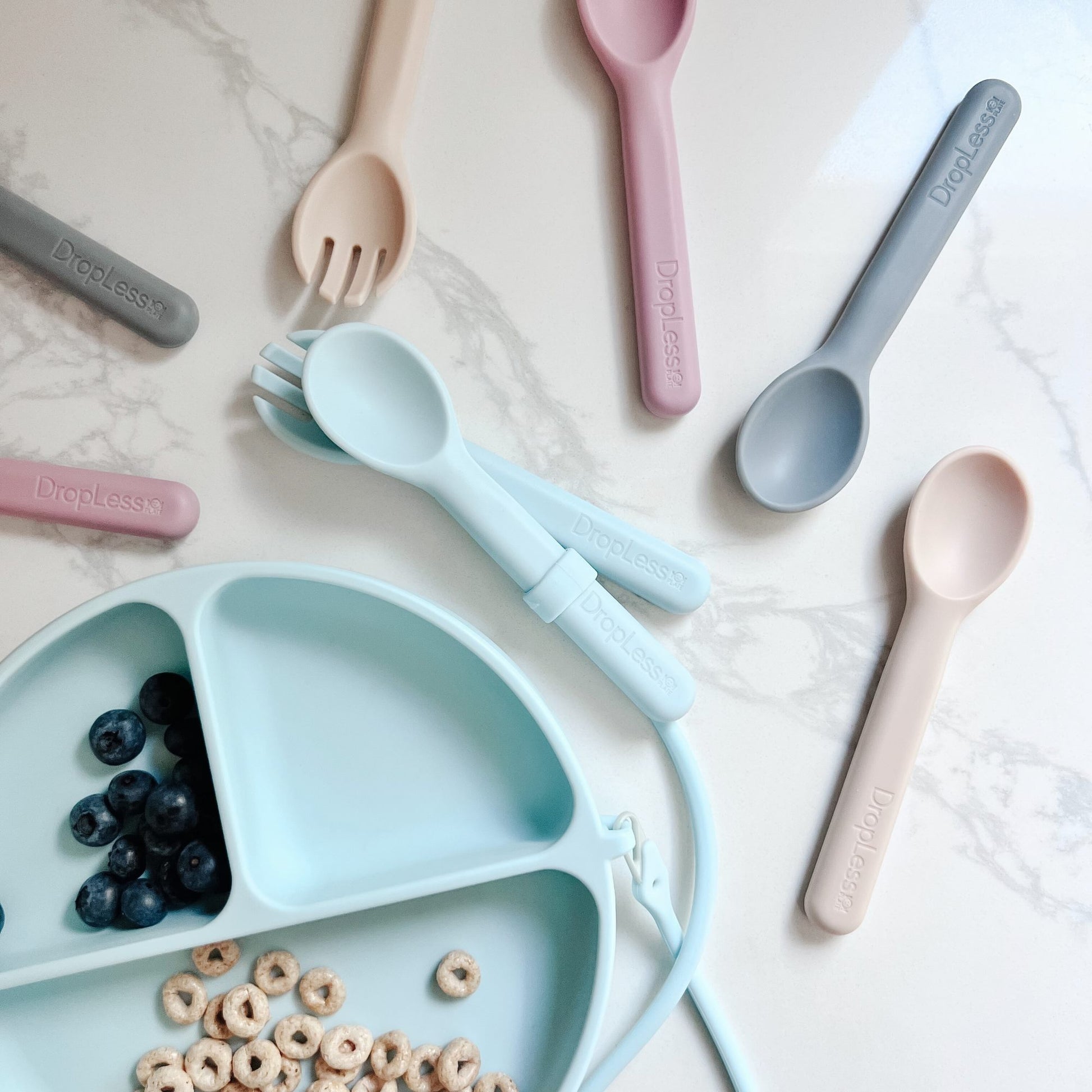 Dropless plate Children's cutlery set with a divided plate containing blueberries and cereal on a light surface.